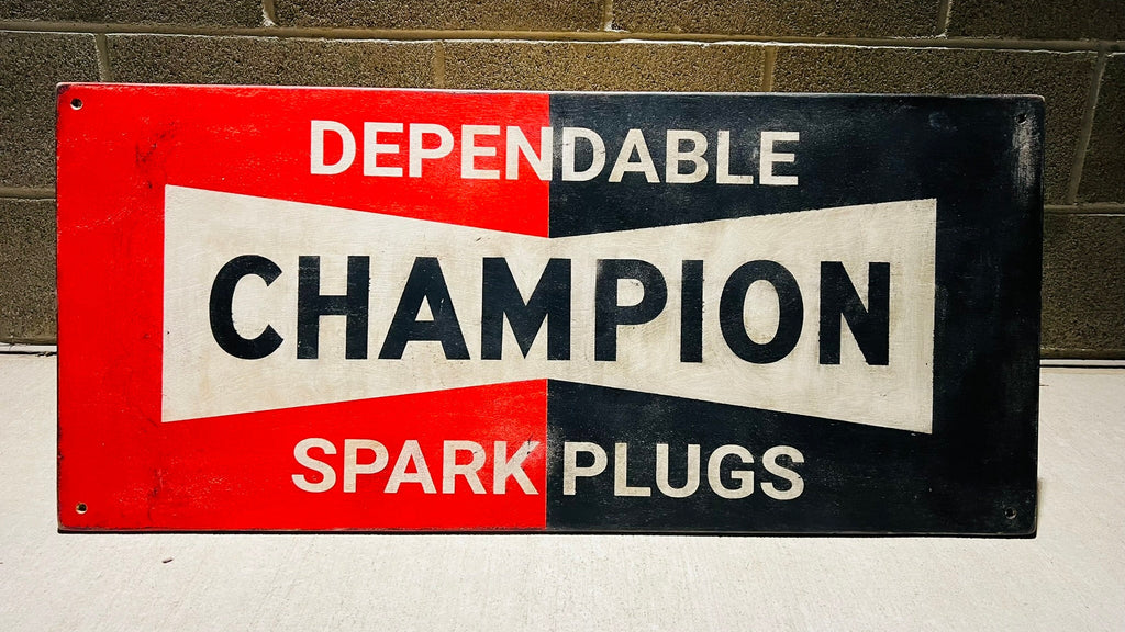 Vintage-style sign for Champion Spark Plugs against a brick wall.