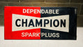 Vintage-style sign for Champion Spark Plugs against a brick wall.