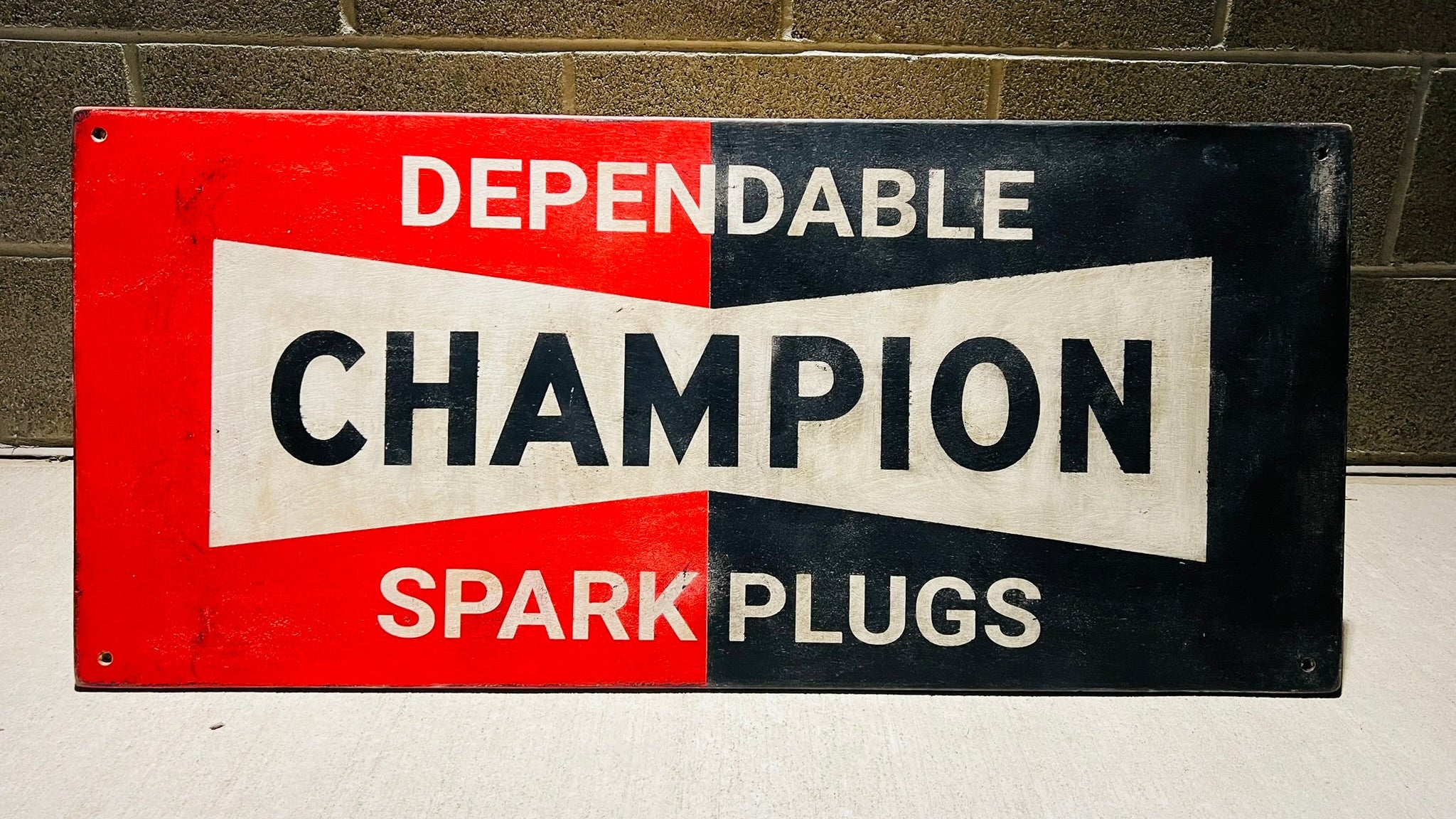 Vintage-style sign for Champion Spark Plugs against a brick wall.
