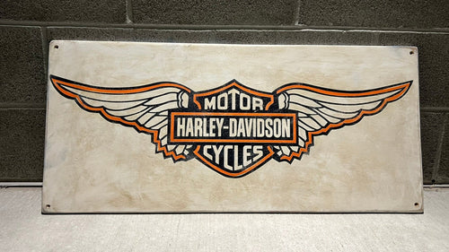 Harley-Davidson logo on a wood sign against a brick wall.