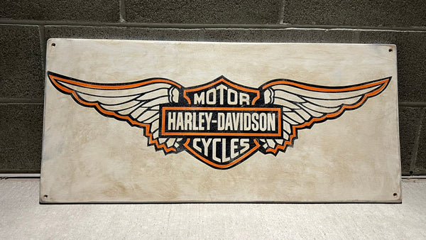 Harley-Davidson logo on a wood sign against a brick wall.